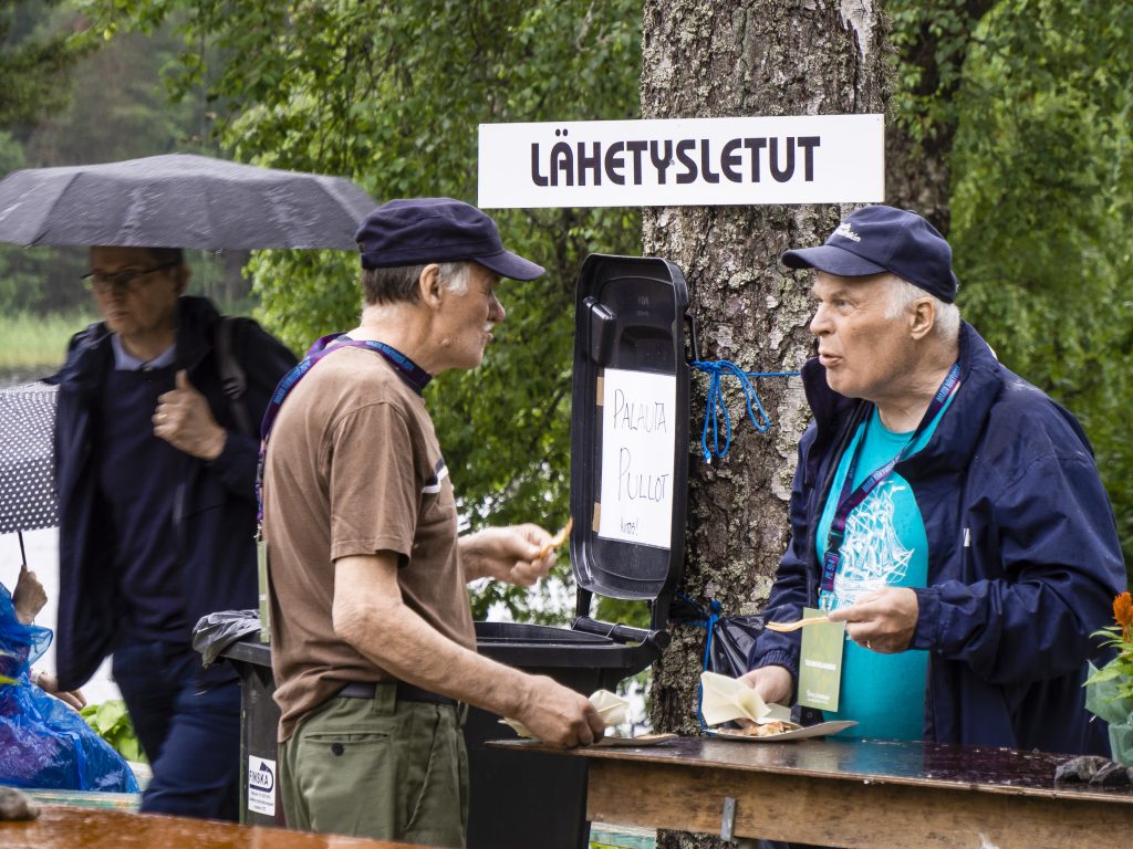 Kaksi vanhaa miestä lippalakit päässä paistaa ja maistaa lettuja.