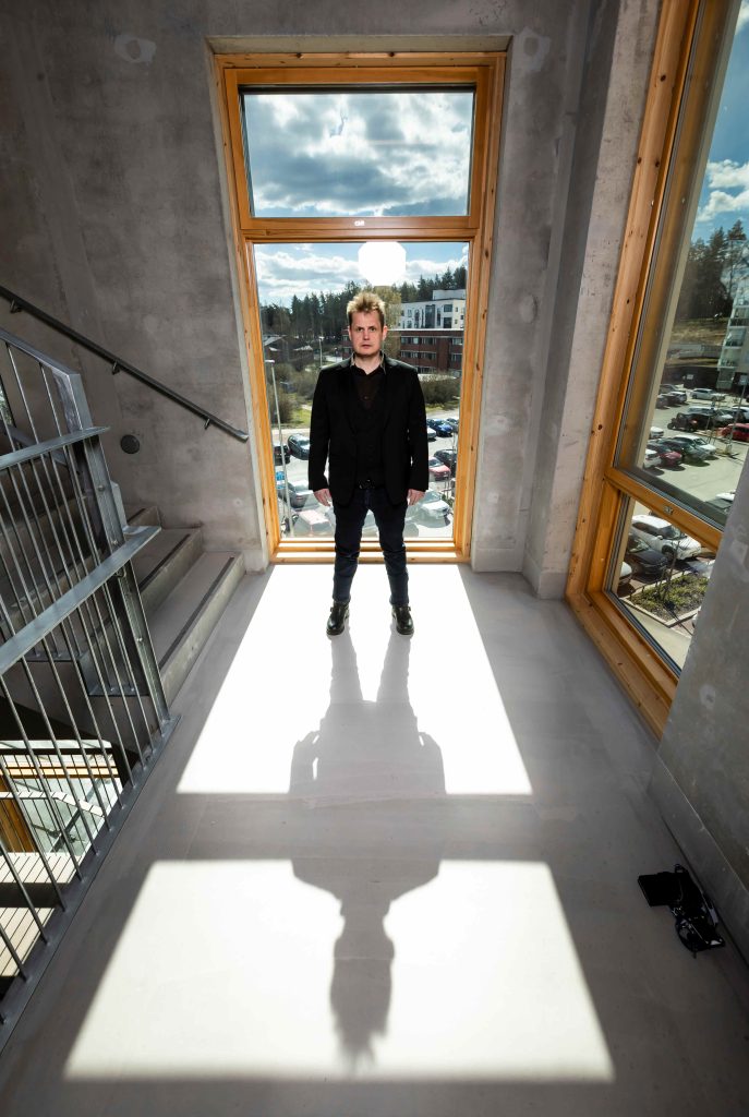 Kuvassa mies seisoo ison ikkunan edessä ja eteen vaalealle käytävälle lankeaa hänen varjonsa.