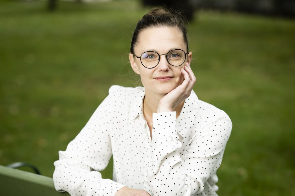 Kuvassa puolilähikuva silmälasipäisestä naisesta jolla on valkoinen paita.