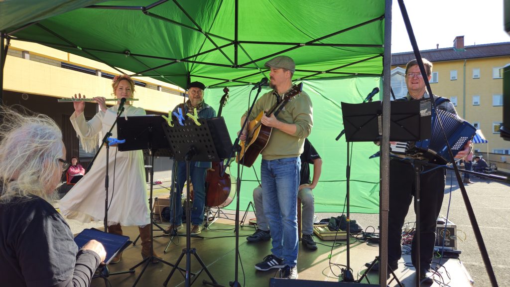 Kuvassa on laulu- ja soitinyhtye lavalla