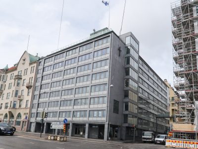 Harmaa yhdeksänkerroksinen laatikkomainen toimistorakennus jonka seinässä on risti.