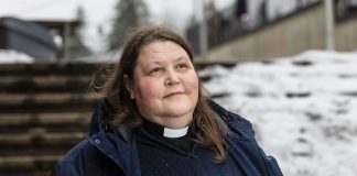 Kirkkoherra Ulla Kosonen: ”Hengellinen tieni on tavanomainen ja tylsä, mutta sen varrella on ollut paljon upeita kukkaketoja” Pitkätukkainen nainen papin tunnukset kaulassa seisoo lumisen aidan edessä.