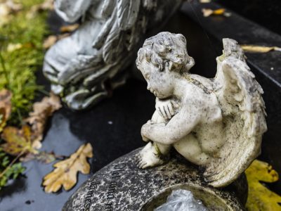 Kivinen pieni enkeli kyyhöttää kyyryssä hautakiven päällä