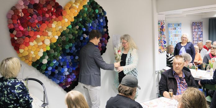 Vesa Koivisto kukittaa Hanna Mäntysen Kirkkoherra Vesa Koivisto ojentaa kukat ryijyn ideoineelle Hanna Mäntyselle. Takana seinällä värikäs ryijy.