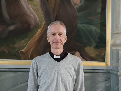 mies seisoo alttaritaulun edessä ja katsoo suoraan kameraan