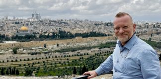 Etualalla mies katsoo kameraan ja taustalla näkyy vanhaa kaupunkimaisemaa