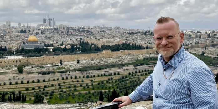 Etualalla mies katsoo kameraan ja taustalla näkyy vanhaa kaupunkimaisemaa