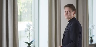 mies seisoo ikkunan edessä ja katsoon kameraan