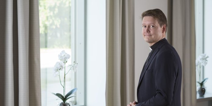 mies seisoo ikkunan edessä ja katsoon kameraan