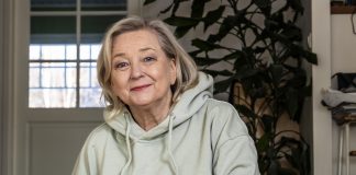 Kolumni: Saarnamiehen tytärtä kannetaan kotiin asti Kuvassa nainen istuu huppari yllään ja hymyilee kameralle.