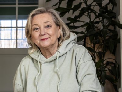 Kuvassa nainen istuu huppari yllään ja hymyilee kameralle.