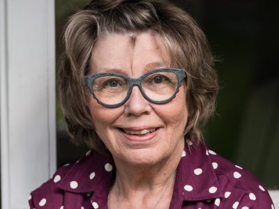 Lähikuvassa nainen jolla on silmälasit ja hän katsoo hymyillen kameraan.