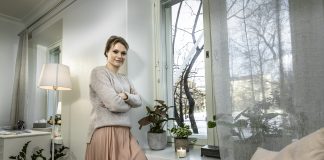 Nainen nojaa olohuoneessa ikkunan pieleen. Ikkunalaudall palaa kynttilä.