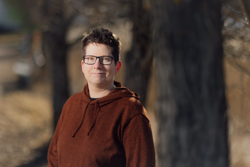 Lyhyttukkainen, silmälasipäinen nainen seisoo tummaa taustaa vasten.