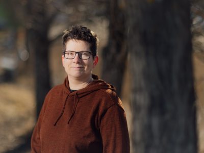Lyhyttukkainen, silmälasipäinen nainen seisoo tummaa taustaa vasten.