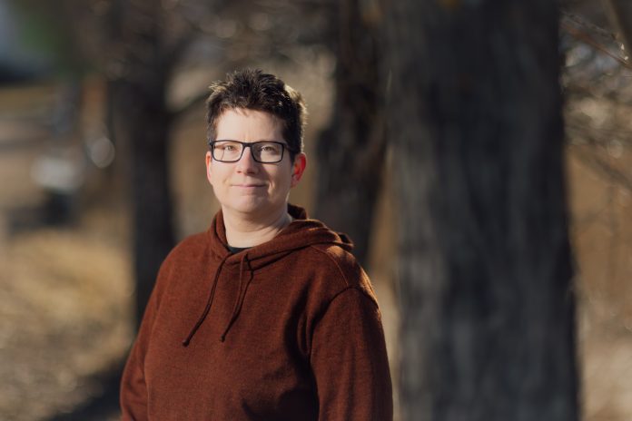 Lyhyttukkainen, silmälasipäinen nainen seisoo tummaa taustaa vasten.