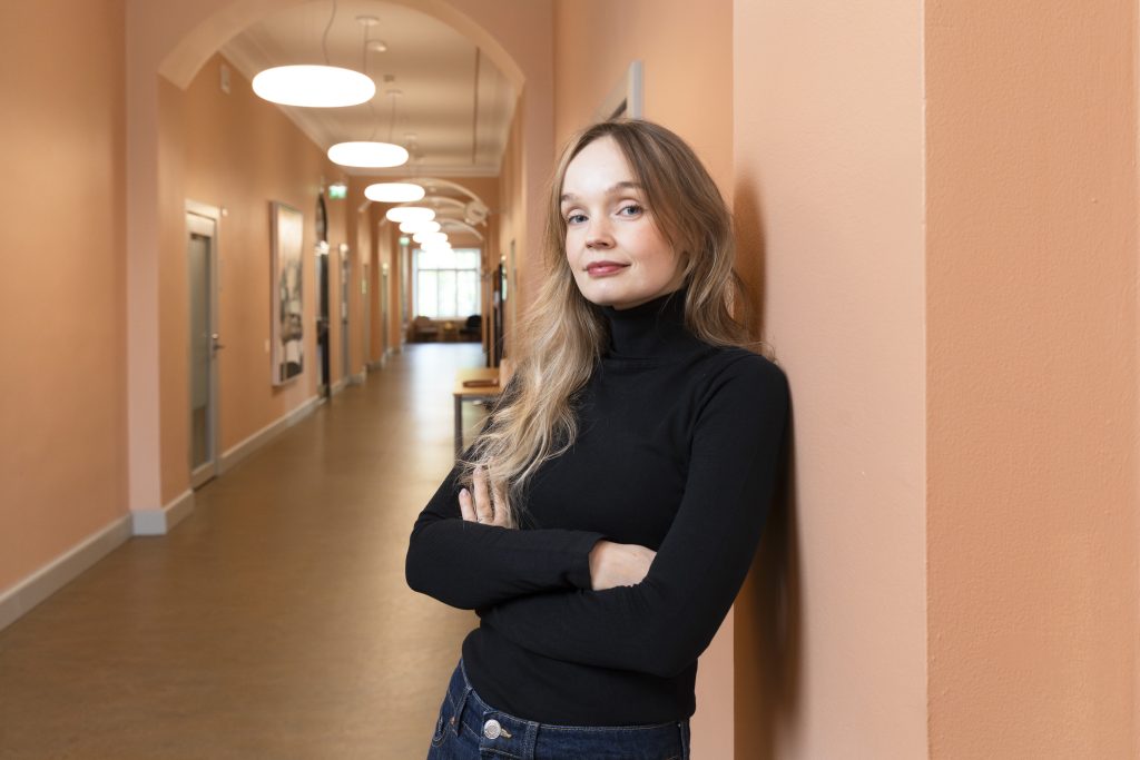 Nainen nojaa seinään käytävällä kädet puuskassa.