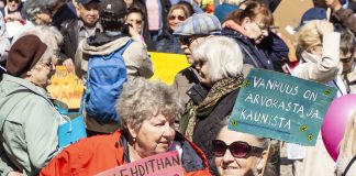 Ihmisjoukko osoittaa mieltään. Etualalla kaksi naista kyltteineen.