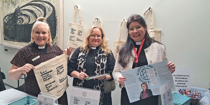 kolme naista katsoo suoraan kameraan ja esittelee markkinointimateriaaleja