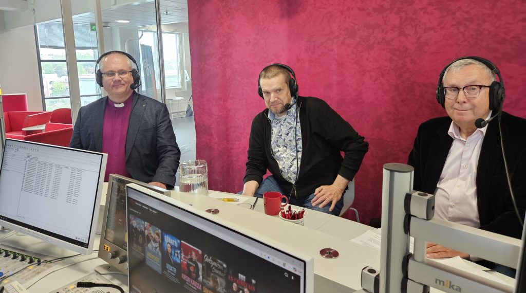 Kuvassa kolme miestä istuu radiostudiossa luurit korvilla