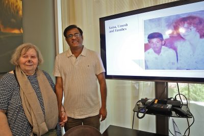 nainen ja mies seisovat monitorin vieressä ja monitorissa heidän kuvansa monen vuosikymmenen takaa