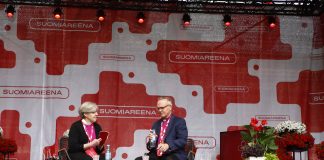 Kaksi violettipaitaista piispaa, nainen ja mies, istuu puhujalavalla.