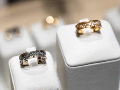 Kaksi kivillä koristeltua sormusta valkoisilla esittelytelineillä koruliikkeen vitriinissä.