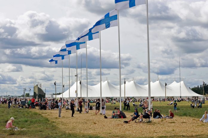 rivi suomen lippuja ja taustalla seurateltta