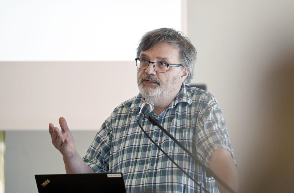 Parrakas silmälasipäinen professori Antti Laato puhuu teologisen symposiumin puhujakorokkeella.