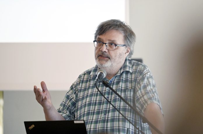 Parrakas silmälasipäinen professori Antti Laato puhuu teologisen symposiumin puhujakorokkeella.