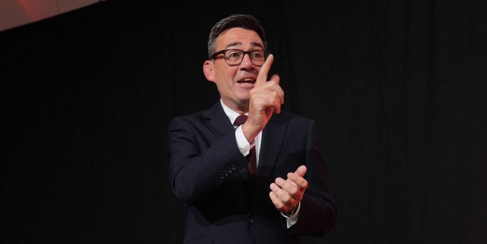 Labour leadership Mies puvussa seisoo elävästi viittoen mustaa taustaa vasten.