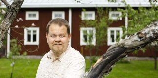 Mies seisoo vanhan pohjalaistalon edessä.