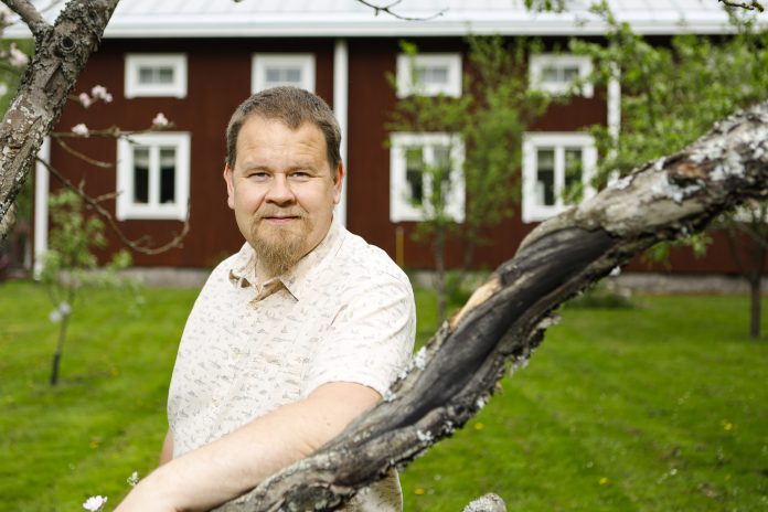 Hiltunen Kalle by Timo Aalto20260604_2350 Mies seisoo vanhan pohjalaistalon edessä.