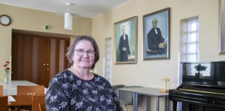 Vuoden 2026 Kirkonpalvelijaksi valitulle Kirsi Romolle toisen auttaminen on työn ydin Silmälasipäinen henkilö istuu pöydän ääressä vaaleassa seurakuntasalissa ja katsoo kameraan. Taustalla näkyy musta piano, pieni puinen risti sekä seinällä kaksi kehystettyä muotokuvaa. Vasemmalla on pöytiä, tuoleja ja puiset pariovet.