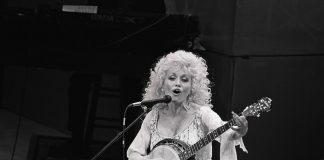 Dolly Parton oli avoin hengellisyydestään: ”Minusta meidän täytyy uskoa johonkin meitä itseämme suurempaan ja parempaan” Mustavalkoinen kuva, jossa nainen soittaa banjoa ja laulaa