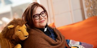 Kehitysvammaistyön pappi Elina Jokipaltio on hymyilevän Jumalan työtoveri Puolilähikuvassa ruskeahiuksinen, silmälasipäinen, hymyilevä nainen istuu oranssilla sohvalla vieressään pehmoleluleijona