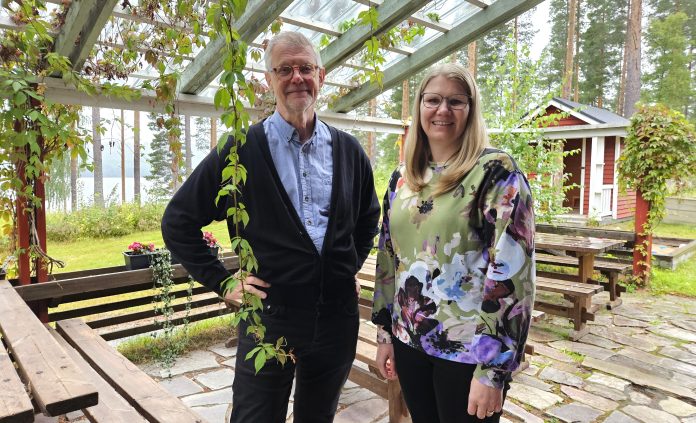 Kari Latvus ja Anne Sumela by Emilia Karhu Kuvassa nainen ja mies seisovat terassilla, jonka katossa kulkee villiviiniä.