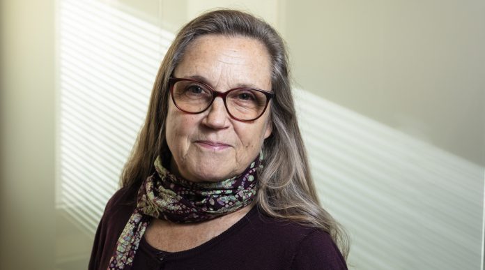 Kaisa Raittila kuvattuna 25.10.2024 Kuvassa puolilähikuva silmälasipäisestä, pitkähiuksisesta naisesta. Taustalla vaalealle seinälle siiloutuu arugingon valoa ikkunasta.