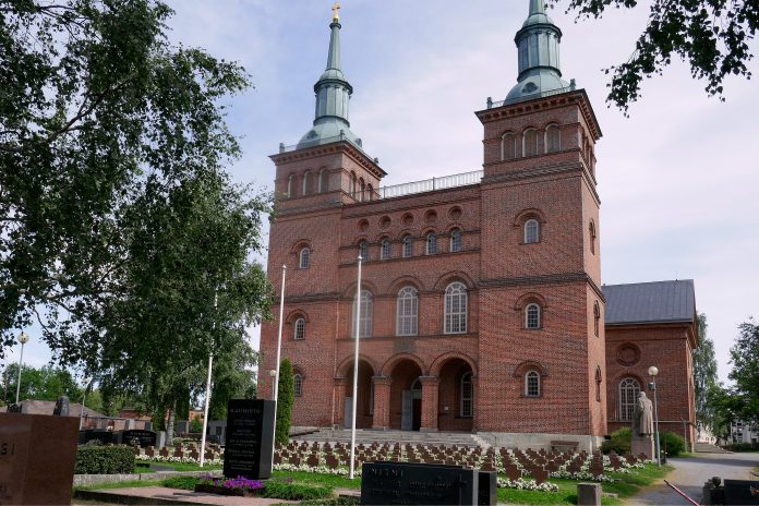 Tyrvään kirkko by Seppo Punatiilinen kirkkorakennus, jossa kaksi tornia, kirkkomaan takana.
