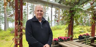 Kuvassa puolilähikuva miehestä jolla on tumma villatakki. Taustalla näkyy puita ja terassin kukkalaatikko.