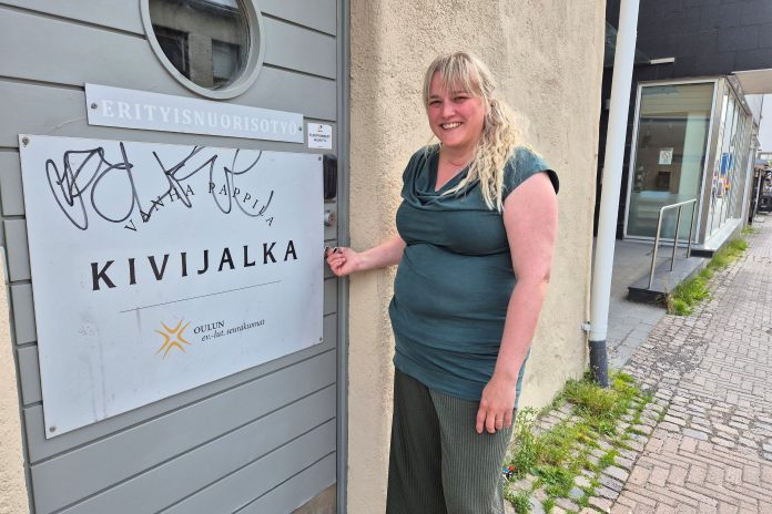 nainen on avaamassa ovea ja katsoo kameraan