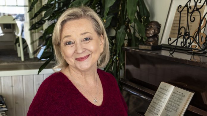 Ekola Hanna-5627by Jukka Granström Puolilähikuvassa vaaleahiuksinen nainen katsoo kameraa ja istuu pianotuolilla hymyillen.