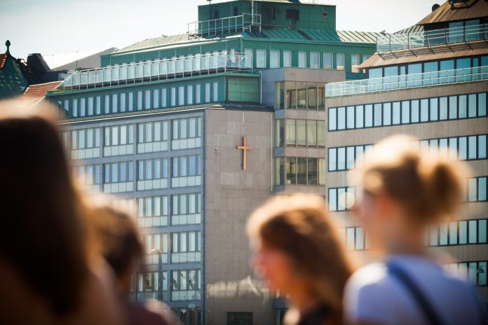 Kirkkohallitus etelaranta-8-kirkkohallitus-tiedotekuva-2409-2026 by Kirkon viestintä Kuvassa Kirkkohallituksen talo kuvattuna Kauppatorilta käsin, etualalla ihmishahmoja.