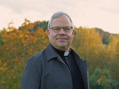 pappismies seisoo ulkona liperit kaulassa ja katsoo suoraan kameraan