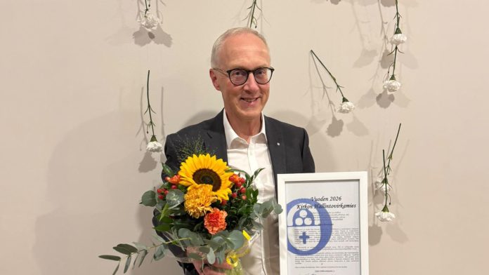 Pasi Perander Vuoden KiHV 2026 Kuvaaja Juha Silander Mies seisoo kukkakimppu ja kunniakirja käsissään. Hymyilee.