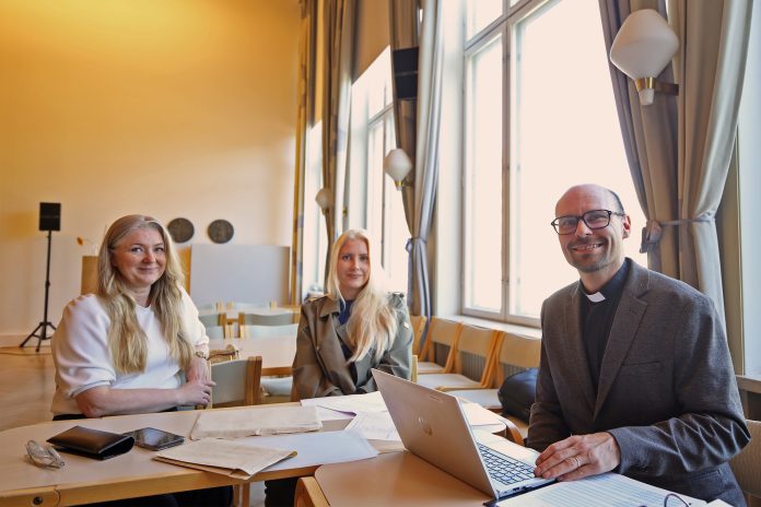 Turun srk vaalilistat kaksi naista ja pappismies istuvat pöydän ääressä ja katsovat kameraan