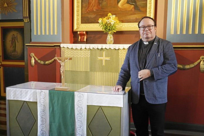 Mies seisoo alttarin edessä ja katsoon suoraan kameraan
