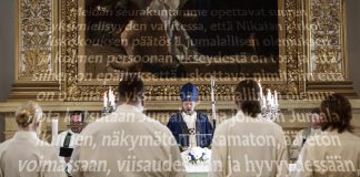 Tunnustuskirjojen käyttö on niin vähäistä, etteivät papitkaan tunne niiden sisältöä – syytä olisi, sanovat asiantuntijat Kirkossa toimitettava jumalanpalvelus. Alttarin edessä seisoo vaaleisiin asuihin pukeutuneita henkilöitä, ja keskellä pappi lukee alttarilta. Taustalla on suuri kehystetty maalaus ja kynttilöitä. Kuvan päällä kulkee suurikokoista, osittain läpikuultavaa suomenkielistä tekstiä.