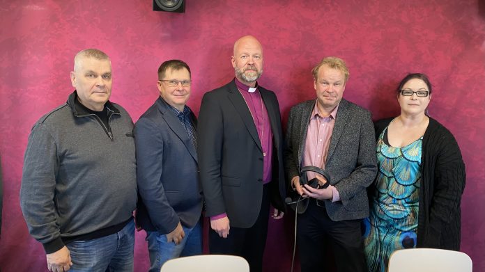 piispa laajasalo kyselytunnilla by radio dei Viisi henkilöä seisoo punaise taustan edelssä. Keskimmäisellä piispan violetti paita.
