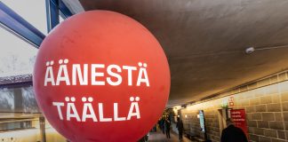 Näkökulma: Kirkon säästöpaineet näkyvät puolueiden vaaliohjelmissa Suuri punainen ilmapallo, jossa lukee ”Äänestä täällä”, vaalipaikan käytävällä. Taustalla ihmiset kulkevat käytävää pitkin.